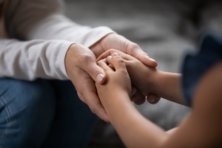 Adult hands holding a child's hands in a comforting gesture